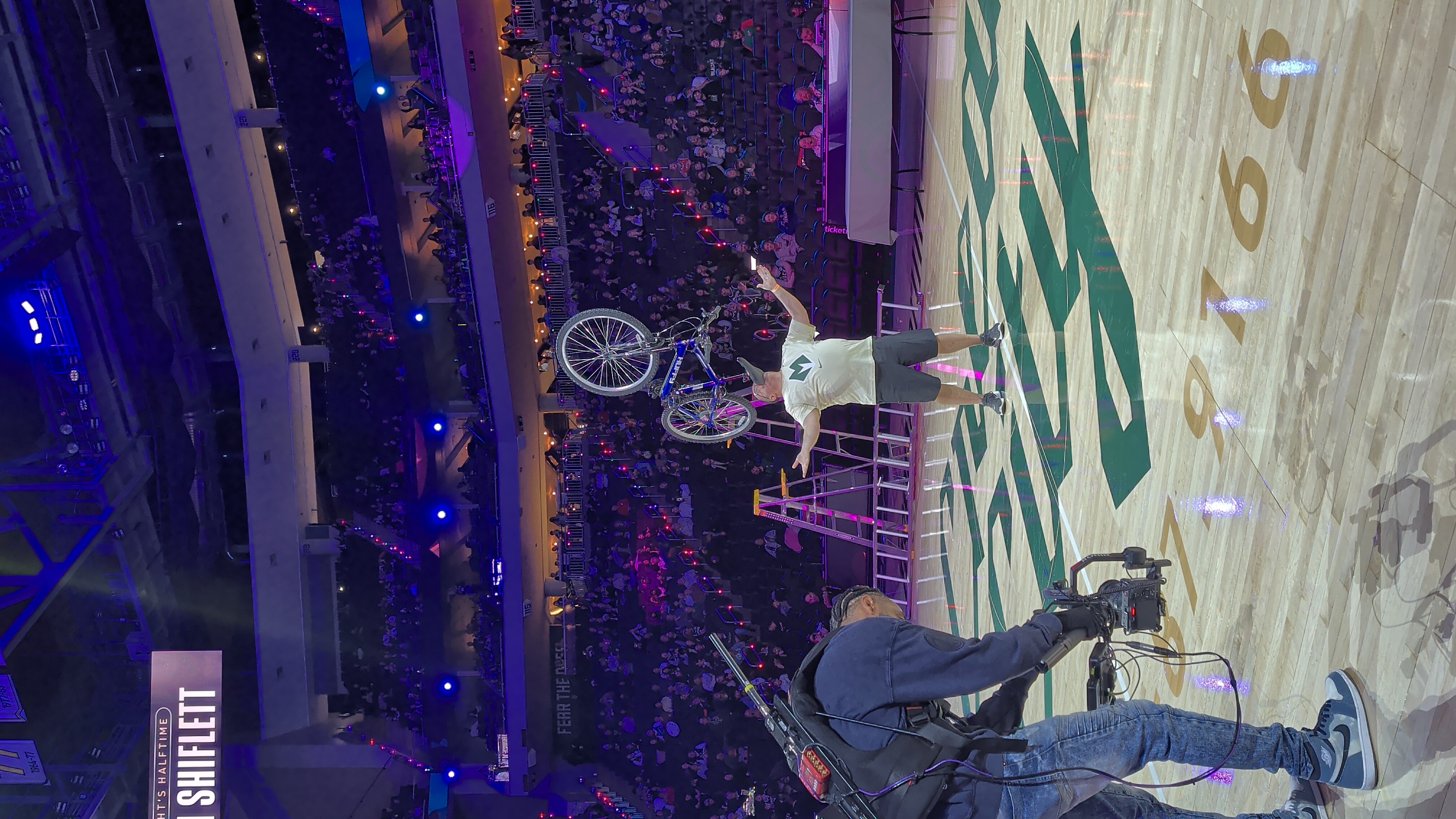 Kevin Shiflett balancing bicycle on his chin at basketball arena halftime show